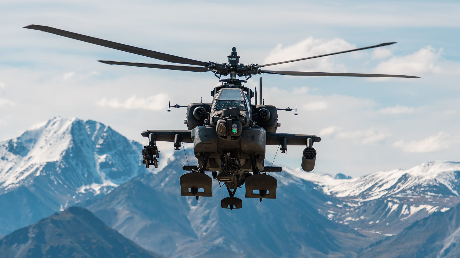 An Apache helicopter with snow-capped mountains in the background