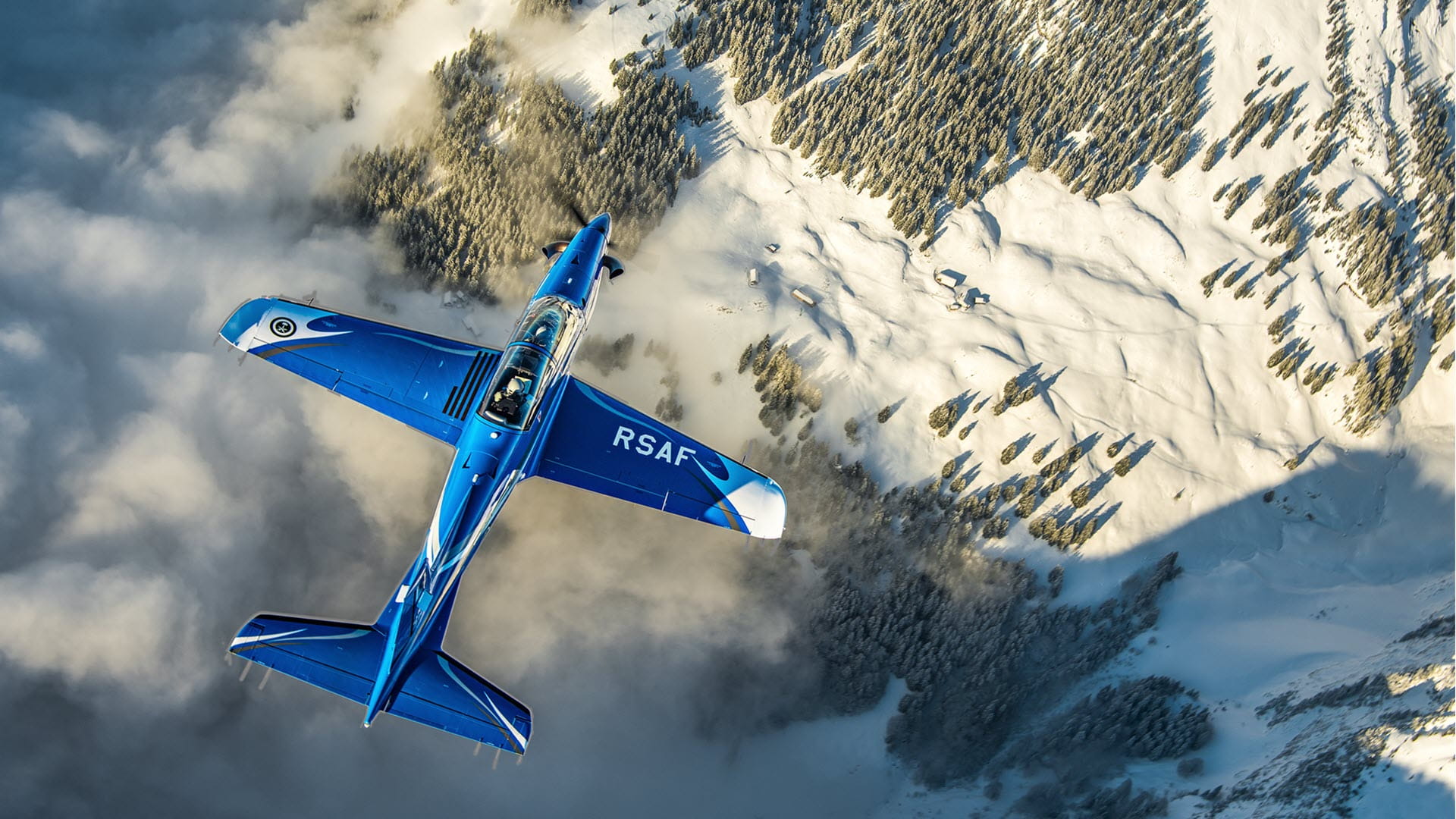 Top-down view of a PC-21 flying over mountains