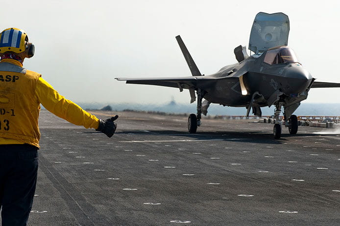 Jet landing on the deck of a ship with a crewman giving the thumbs up.