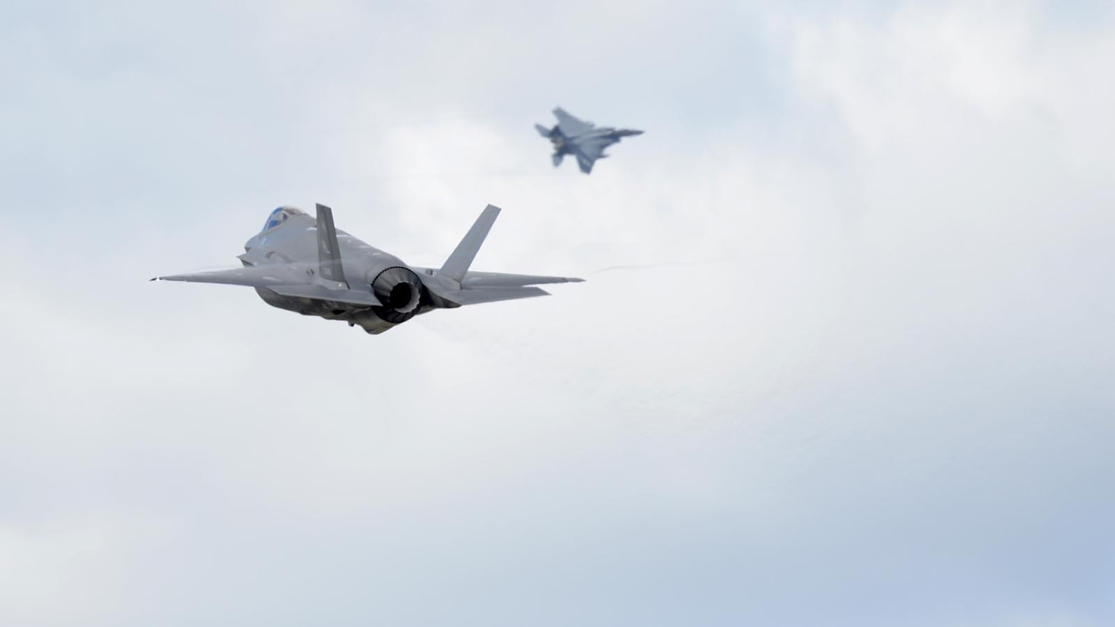 Samolot F-35 Sił Powietrznych USA startuje z bazy Królewskich Sił Powietrznych w Lakenheath w Anglii z myśliwcem F-15 w tle. Raytheon Technologies opracowuje technologie, które pozwolą na współpracę między myśliwcami różnych generacji. (Fot. U.S. Air Force)