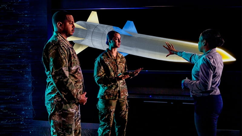 People stand in front of a digital display of a hypersonic weapon concept.