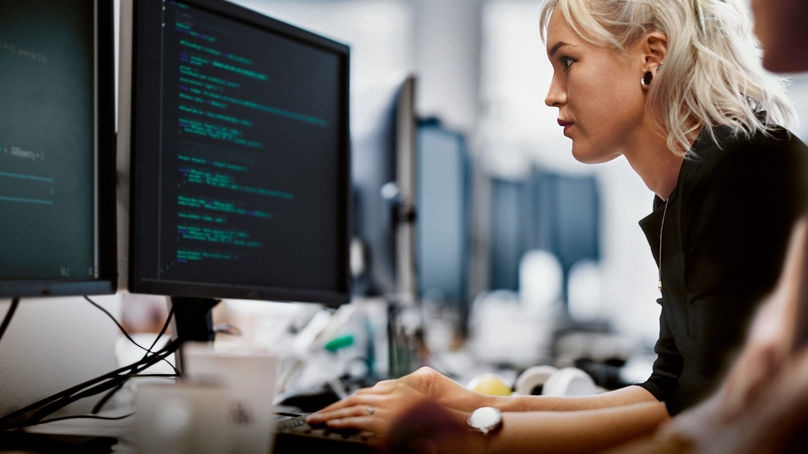 Woman at workstation with code on screen
